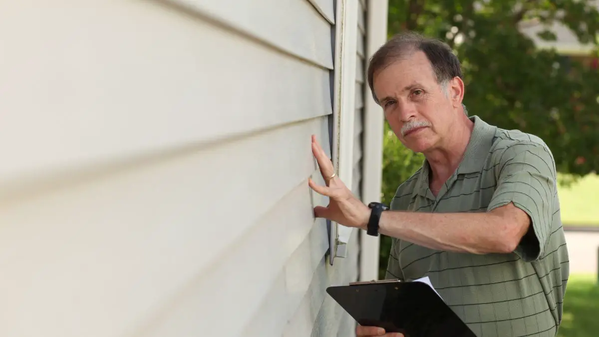 what will fail a VA home inspection - adult male with clipboard inspects vinyl siding on a residential home